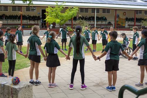 A large group of primary school students standing in a circle and holding hands.