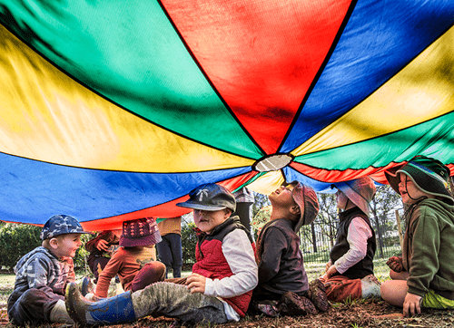 Photo of children playing under colourful parachute.